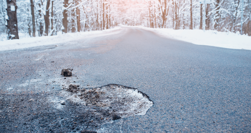 asphalt with pothole and winter trees and snow