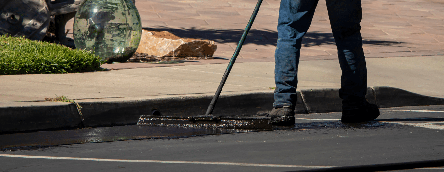 worker using brush to sealcoat asphalt