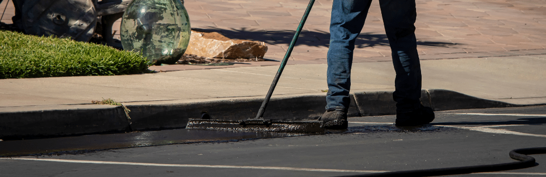 worker using brush to sealcoat asphalt