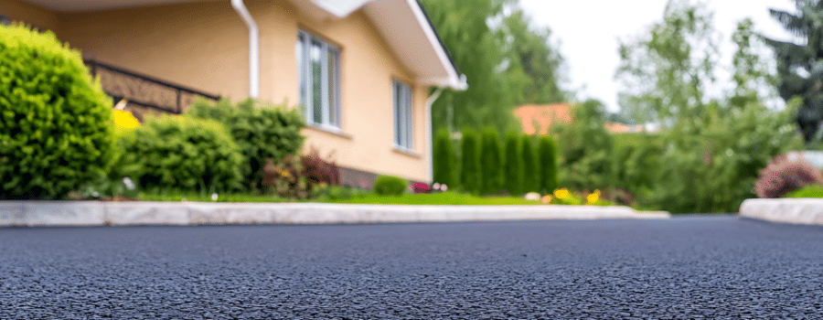 up close of paved asphalt driveway with house and bushes in back